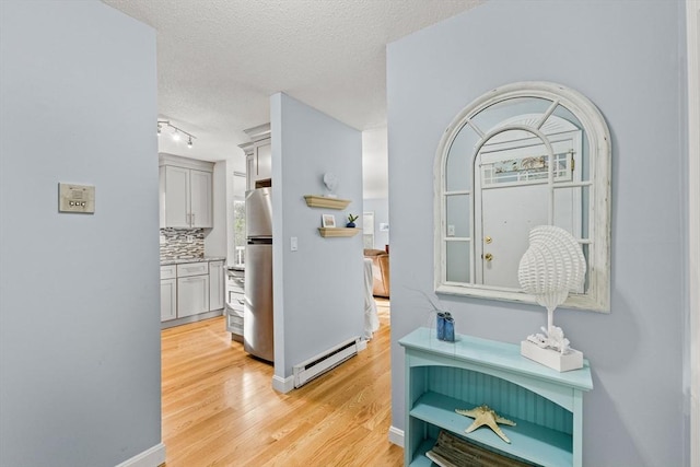 corridor with a textured ceiling, track lighting, baseboard heating, baseboards, and light wood-style floors