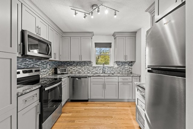 kitchen with a sink, tasteful backsplash, gray cabinetry, appliances with stainless steel finishes, and light stone counters