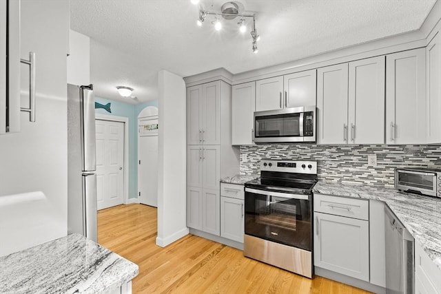 kitchen with a toaster, a textured ceiling, light wood finished floors, stainless steel appliances, and tasteful backsplash
