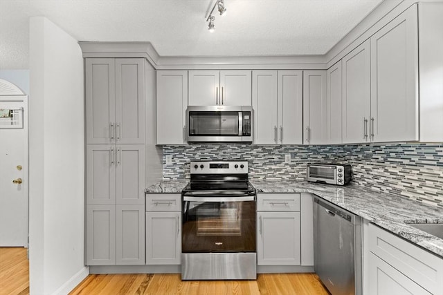 kitchen with light wood-style flooring, gray cabinets, backsplash, appliances with stainless steel finishes, and light stone counters