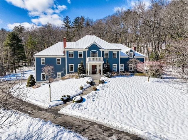 snow covered back of property with a chimney and metal roof