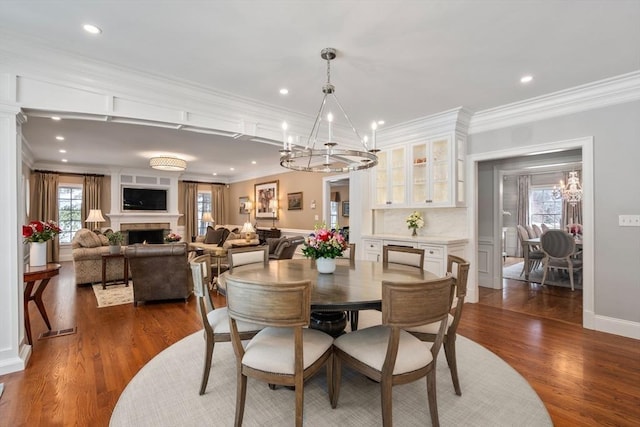 dining area with a lit fireplace, a healthy amount of sunlight, dark wood finished floors, and a notable chandelier