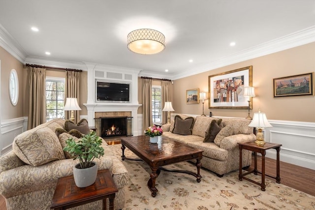 living area featuring light wood-style floors, a wealth of natural light, a wainscoted wall, and ornamental molding