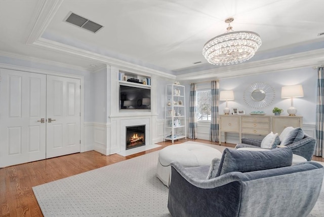 living room with visible vents, ornamental molding, a fireplace with flush hearth, wainscoting, and wood finished floors