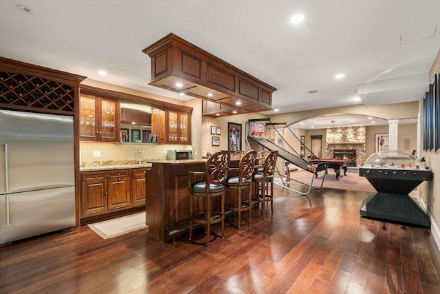 bar featuring arched walkways, dark wood-style flooring, indoor wet bar, a fireplace, and stainless steel built in refrigerator