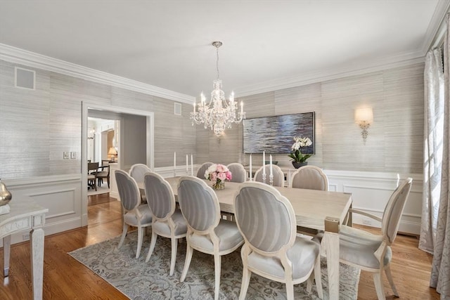 dining area with wallpapered walls, ornamental molding, a chandelier, and wood finished floors