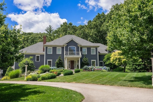 view of front of home with a balcony, a chimney, and a front lawn