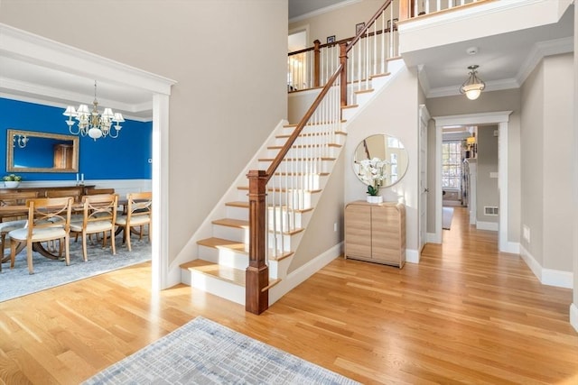 foyer entrance featuring ornamental molding, stairway, wood finished floors, and an inviting chandelier