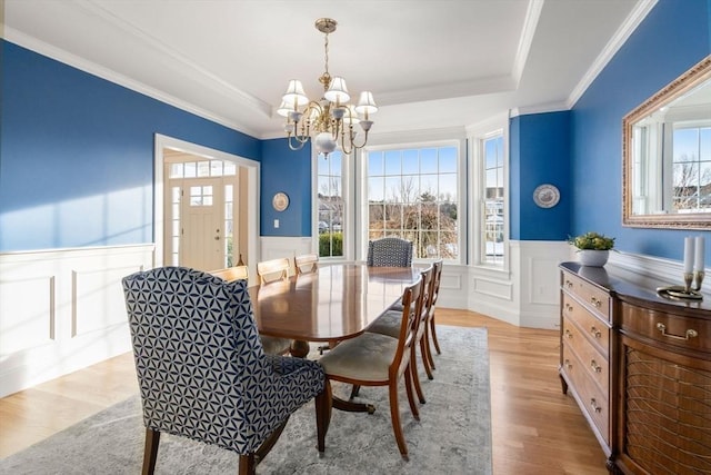 dining area featuring a raised ceiling, a wainscoted wall, ornamental molding, wood finished floors, and a notable chandelier