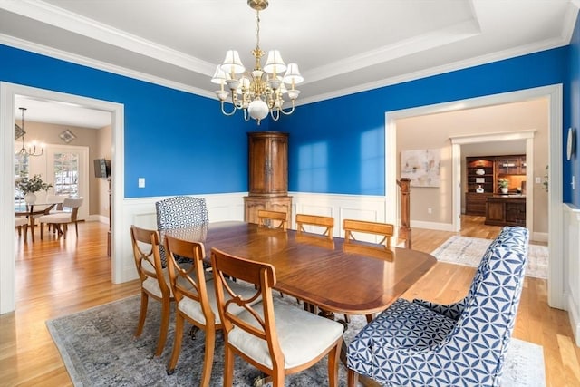 dining area with an inviting chandelier, a tray ceiling, light wood finished floors, and wainscoting