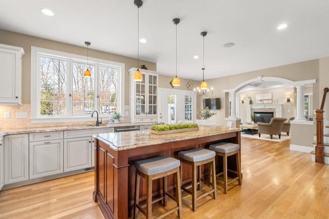 kitchen with decorative columns, a glass covered fireplace, light stone counters, open floor plan, and a center island