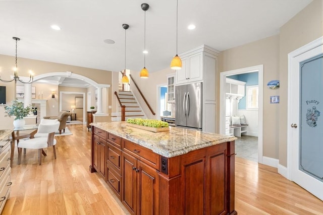 kitchen with stainless steel fridge, a kitchen island, light stone countertops, light wood-type flooring, and white cabinetry