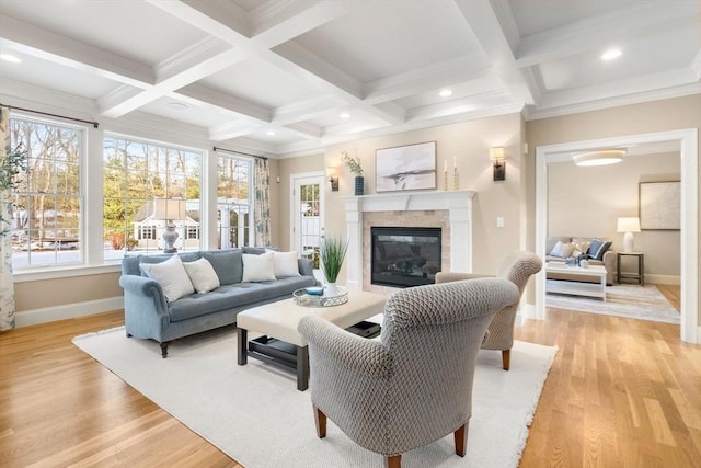 living area with beam ceiling, a glass covered fireplace, a wealth of natural light, and light wood-style floors