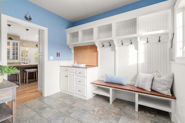 mudroom with a healthy amount of sunlight, a wainscoted wall, and stone finish flooring