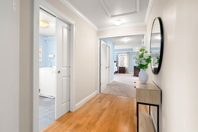 hall with light wood finished floors, baseboards, washer / clothes dryer, crown molding, and a sink