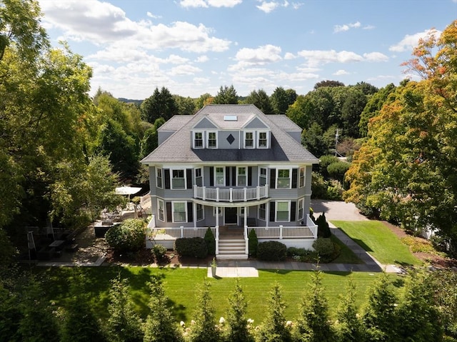 rear view of house featuring covered porch, a lawn, and a balcony