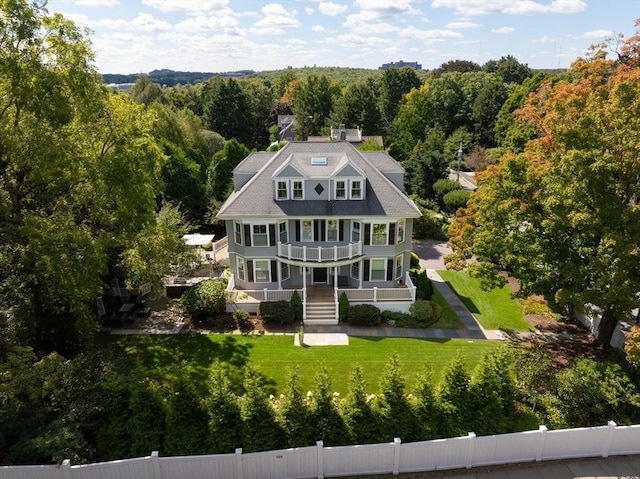 rear view of property with a view of trees, a lawn, a balcony, fence private yard, and a porch