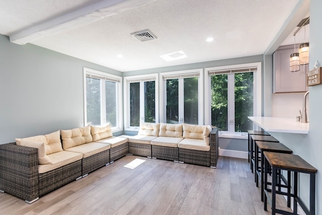 living room with light wood-type flooring, a textured ceiling, and beamed ceiling