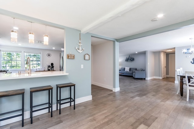 kitchen with hanging light fixtures, hardwood / wood-style floors, sink, a kitchen bar, and beam ceiling