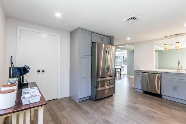 kitchen with gray cabinetry, stainless steel appliances, light hardwood / wood-style floors, sink, and pendant lighting