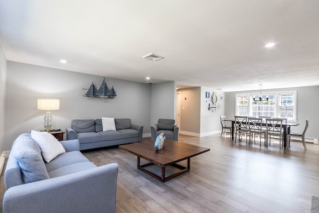 living room featuring a baseboard radiator, an inviting chandelier, a textured ceiling, and light hardwood / wood-style flooring