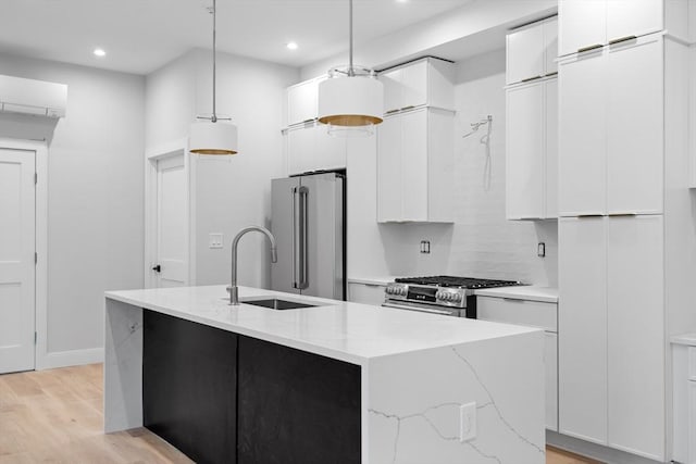 kitchen featuring light wood-style flooring, a kitchen island with sink, stainless steel appliances, a sink, and white cabinets