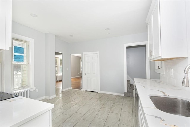 kitchen featuring white cabinets, backsplash, light stone counters, and sink