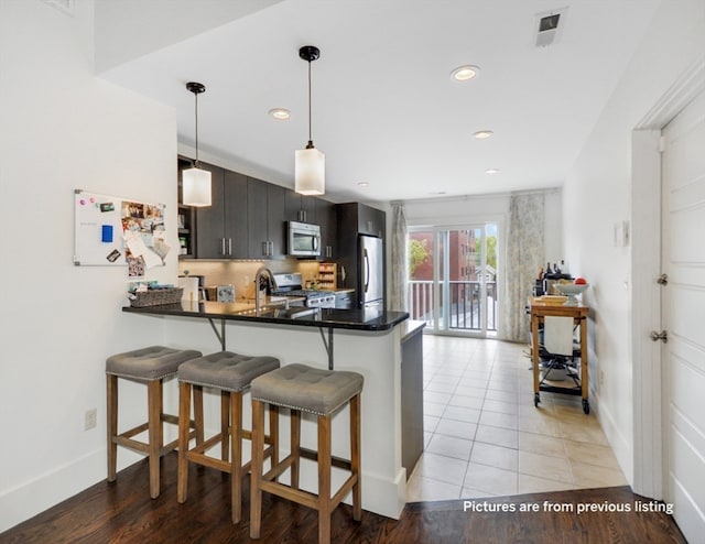 kitchen with kitchen peninsula, appliances with stainless steel finishes, light wood-type flooring, a breakfast bar, and hanging light fixtures