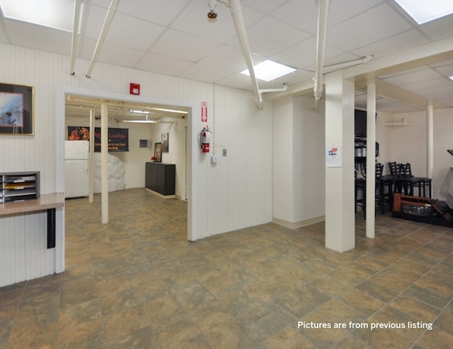 basement with wood walls, a drop ceiling, and white fridge