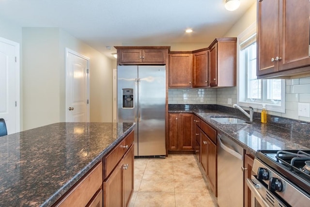 kitchen featuring sink, light tile patterned floors, dark stone countertops, stainless steel appliances, and backsplash