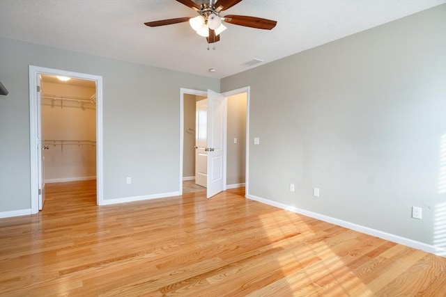 unfurnished bedroom featuring a closet, a walk in closet, ceiling fan, and light hardwood / wood-style flooring