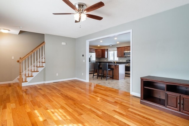 unfurnished living room featuring sink, ceiling fan, and light wood-type flooring