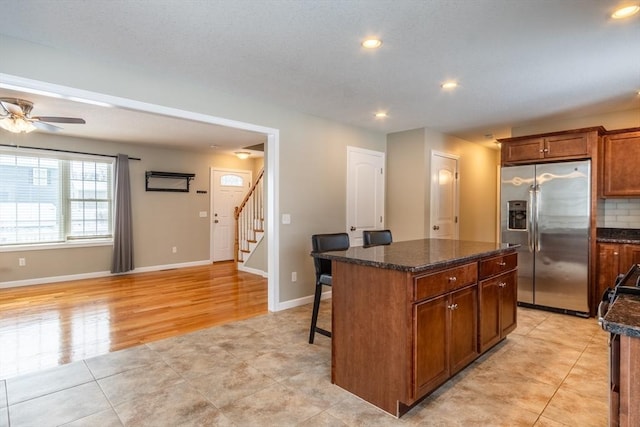 kitchen with light tile patterned flooring, stainless steel fridge, backsplash, dark stone counters, and a center island