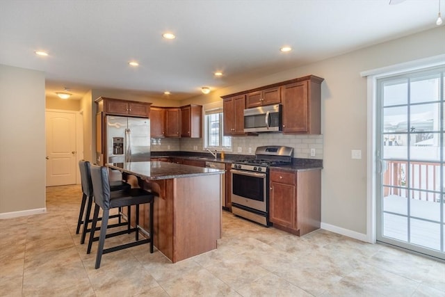 kitchen with a kitchen bar, sink, a center island, appliances with stainless steel finishes, and dark stone counters