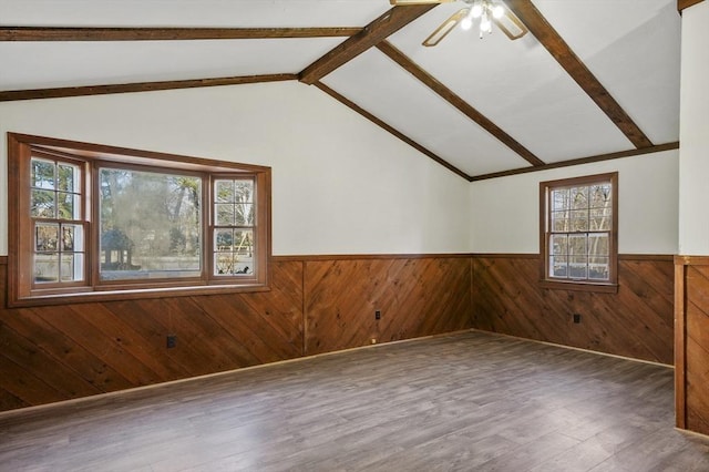 empty room with hardwood / wood-style flooring, a wealth of natural light, lofted ceiling with beams, and wooden walls