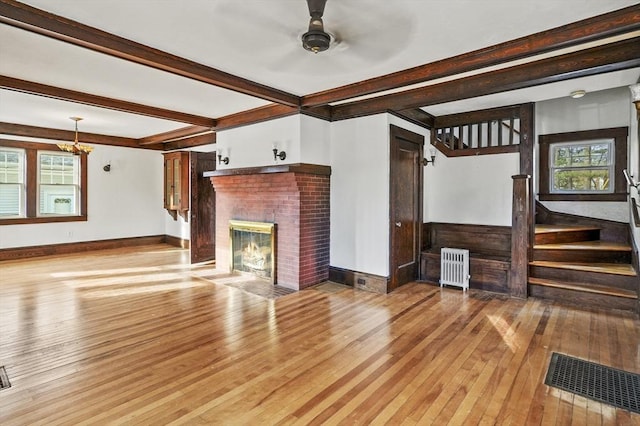 unfurnished living room with a brick fireplace, beamed ceiling, and light wood-type flooring