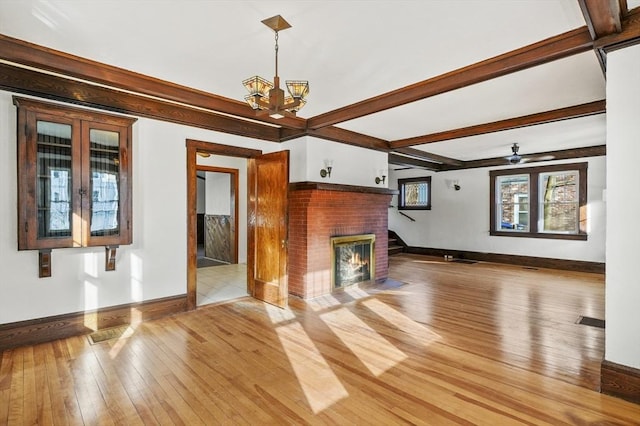 unfurnished living room featuring an inviting chandelier, a fireplace, beamed ceiling, light wood-type flooring, and french doors