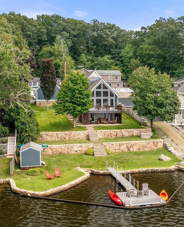 rear view of property with stairway, a deck with water view, and a yard