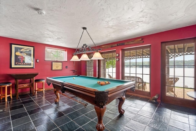 game room with billiards table, a water view, a textured ceiling, and baseboards