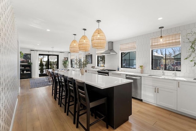 kitchen with a kitchen bar, white cabinetry, pendant lighting, stainless steel appliances, and wall chimney range hood