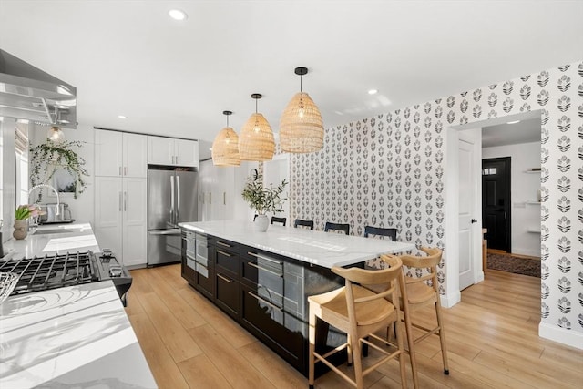 kitchen featuring white cabinetry, hanging light fixtures, light hardwood / wood-style floors, and appliances with stainless steel finishes