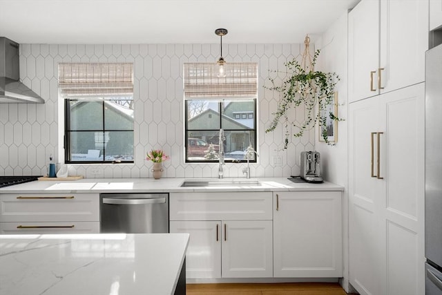 kitchen featuring wall chimney exhaust hood, sink, dishwasher, pendant lighting, and white cabinets