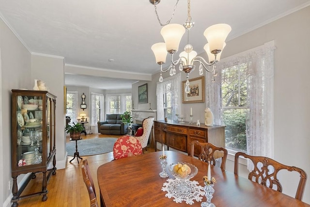 dining room with light wood finished floors, crown molding, a notable chandelier, and baseboards