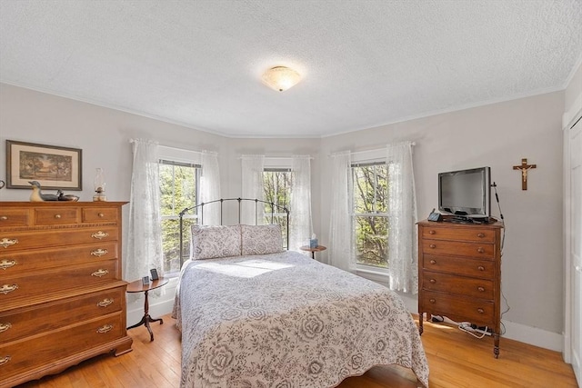bedroom with ornamental molding, multiple windows, light wood-style floors, and a textured ceiling