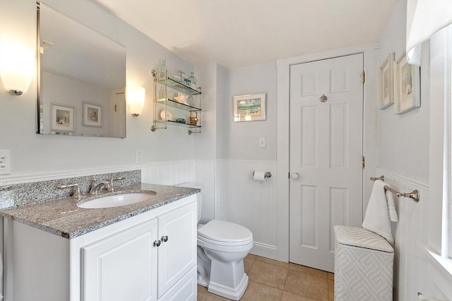 bathroom featuring a wainscoted wall, toilet, tile patterned flooring, and vanity