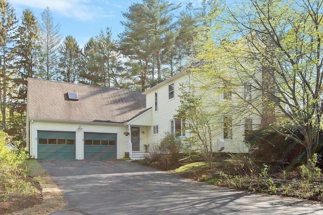 traditional home featuring an attached garage, a shingled roof, and driveway