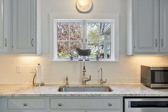 kitchen with a sink, stainless steel microwave, decorative backsplash, and dishwasher