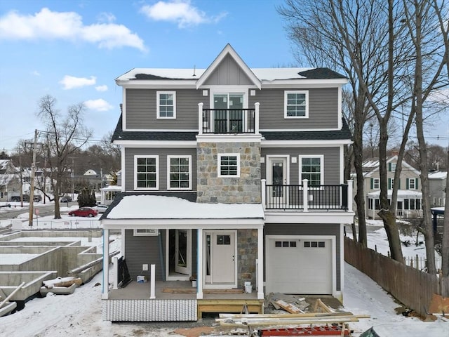 view of front facade featuring fence, stone siding, a balcony, a porch, and a garage