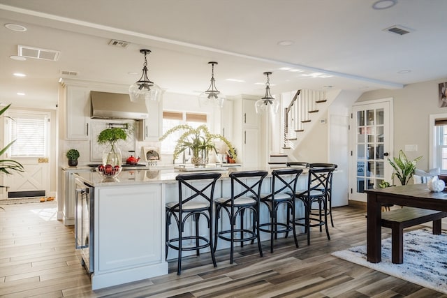 kitchen featuring dark wood-type flooring, white cabinets, tasteful backsplash, wall chimney range hood, and decorative light fixtures