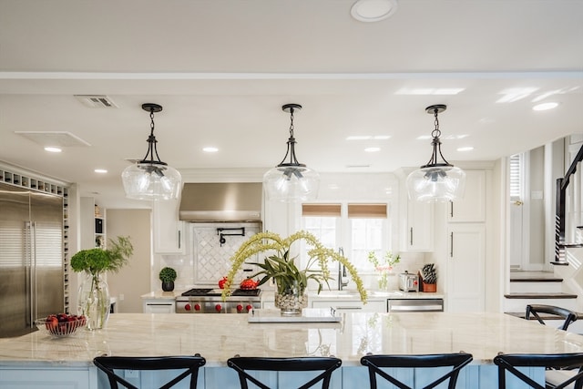 kitchen featuring white cabinets, decorative backsplash, wall chimney exhaust hood, and light stone countertops